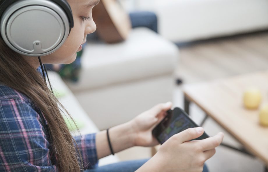 Girl wearing headphones playing a mobile game, representing immersive adaptive game audio technology.